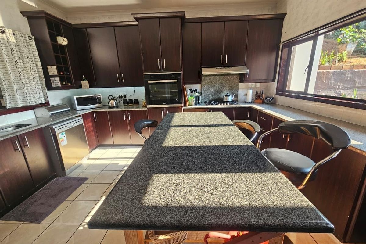 A functional kitchen featuring dark wood cabinetry, granite countertops, a central island, and built-in appliances, offering a classic layout with ample storage space.