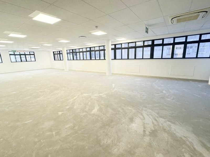 A spacious, open-plan office area featuring a suspended ceiling, recessed lighting, ducted air conditioning, and large windows providing ample natural light.