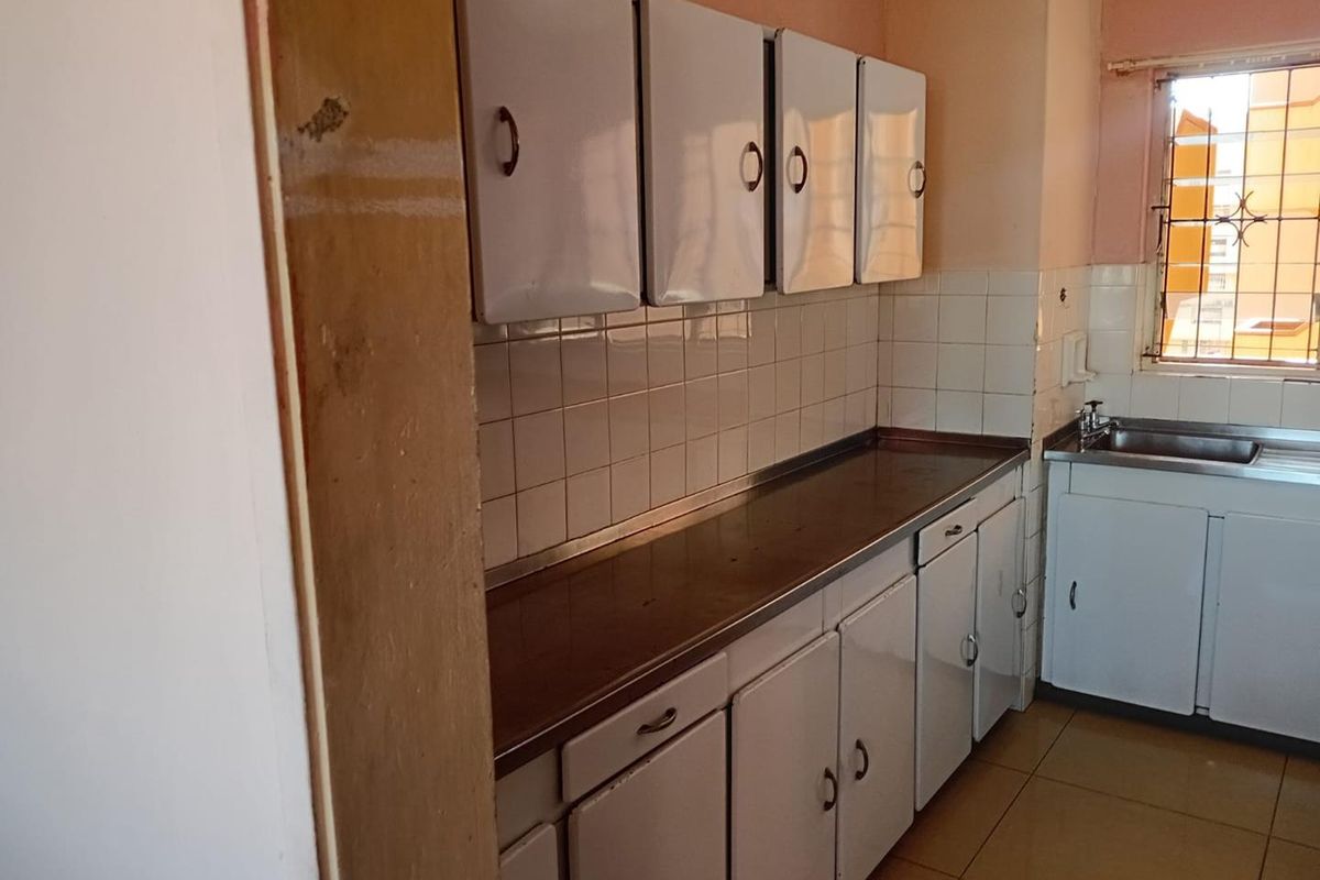 A functional kitchen area featuring white cabinetry, a stainless steel countertop, and tiled splashbacks, offering a practical layout for daily meal preparation.