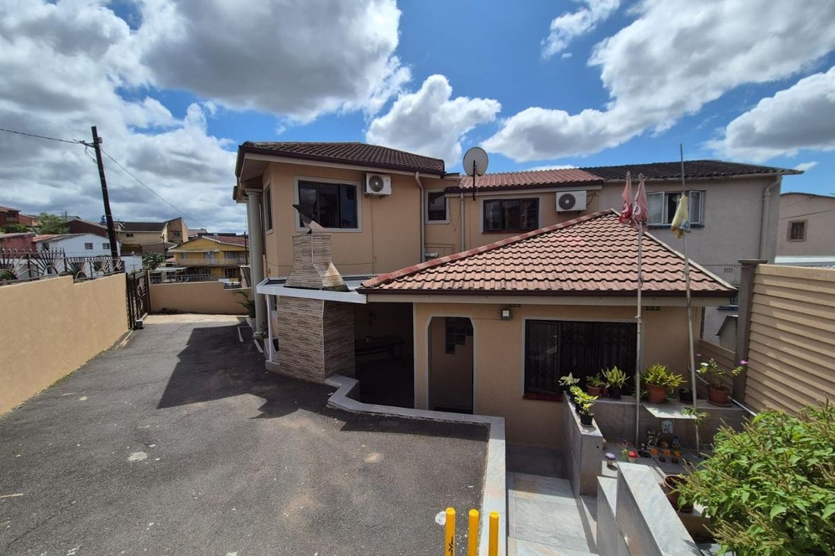 Rear exterior view of the property featuring a paved driveway, built-in outdoor fireplace, and multi-level tiled roof structure.