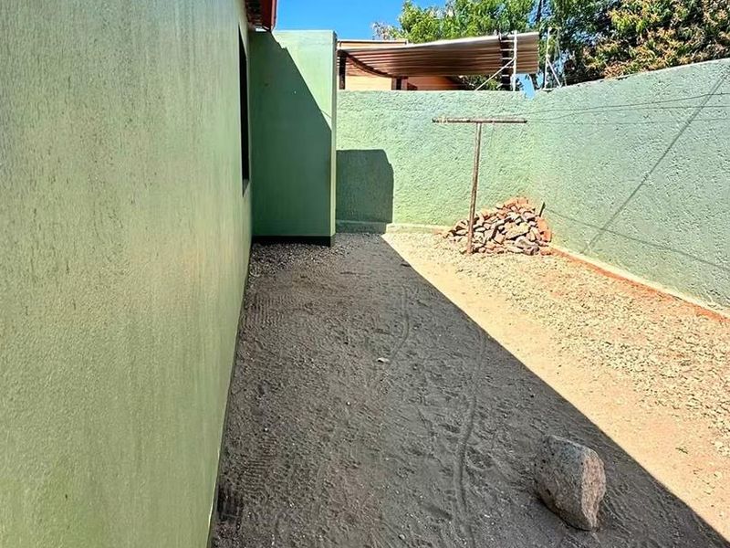 A side or rear yard area featuring a boundary wall, fixed washing line, and unpaved ground surface.