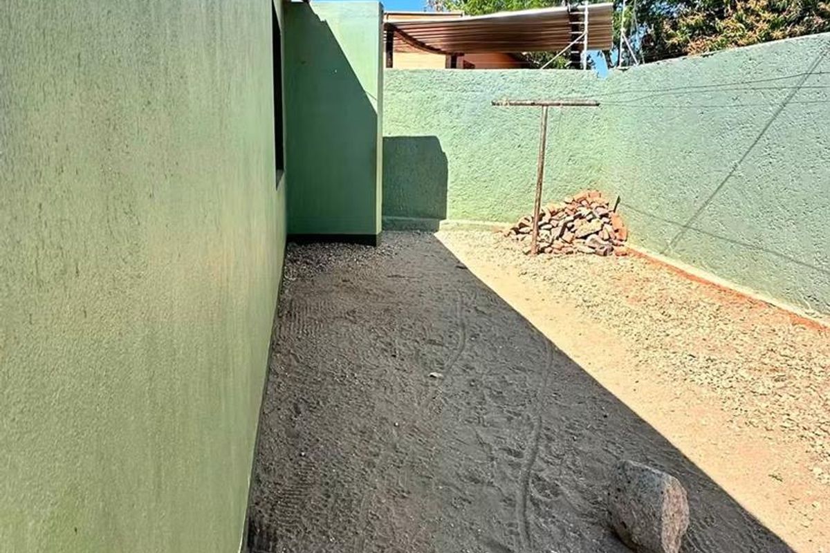 A side or rear yard area featuring a boundary wall, fixed washing line, and unpaved ground surface.