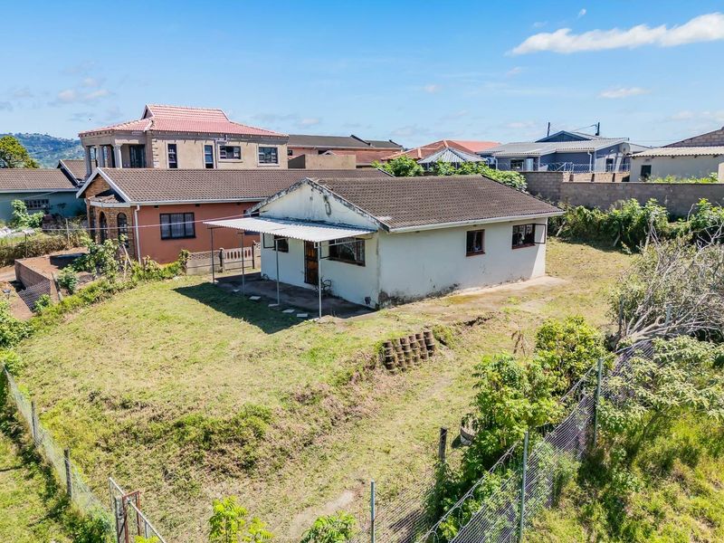 Aerial view of a residential property featuring a detached house with a tiled roof, covered patio, and surrounding garden area on a sloped plot.