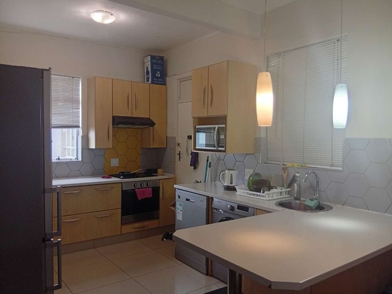 A functional kitchen featuring light wood cabinetry, hexagonal tiled backsplash, built-in oven and hob, and a breakfast bar area with pendant lighting.