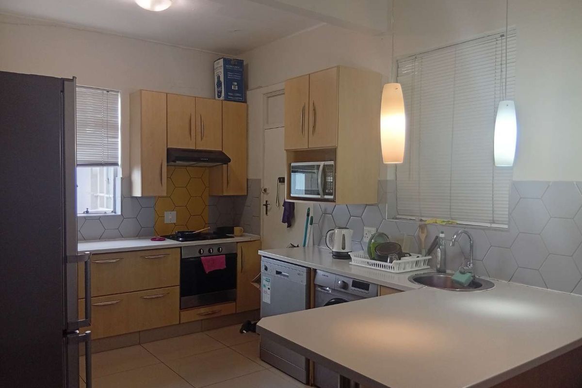 A functional kitchen featuring light wood cabinetry, hexagonal tiled backsplash, built-in oven and hob, and a breakfast bar area with pendant lighting.