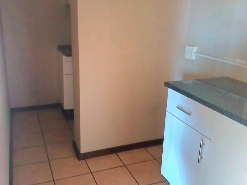 A compact kitchen area featuring built-in cabinetry with stone countertops and ceramic floor tiles, offering a functional layout for office utility needs.