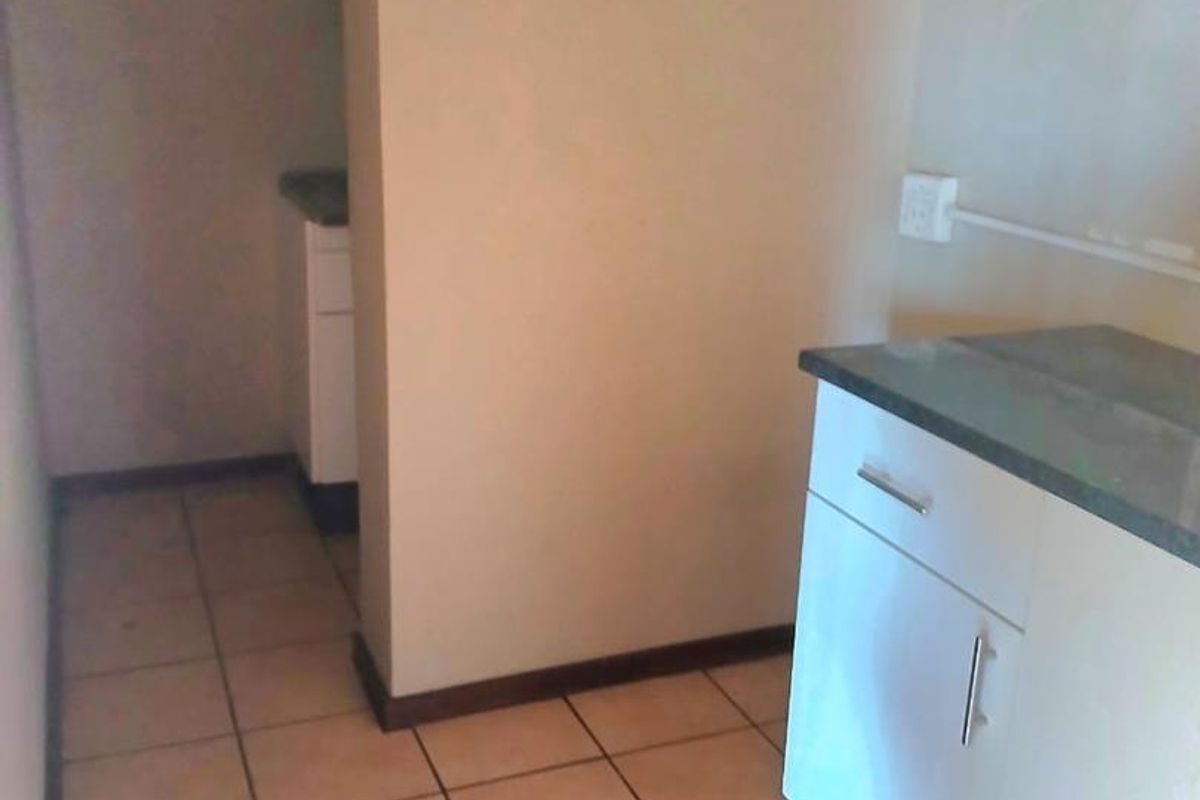 A compact kitchen area featuring built-in cabinetry with stone countertops and ceramic floor tiles, offering a functional layout for office utility needs.