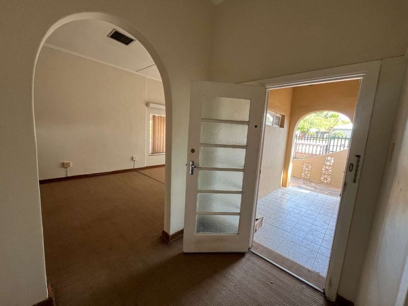 An empty entrance area featuring an arched doorway leading to an interior room and a glass-panelled door opening onto a tiled patio.