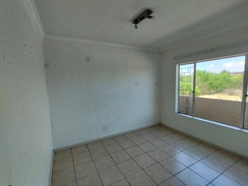 An empty bedroom featuring tiled flooring, security bars on the window, and a ceiling light fixture. The walls require repainting.