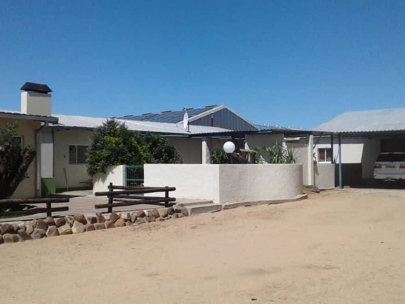 Front exterior view of the industrial property featuring a carport, solar panel installation, and a stone retaining wall.