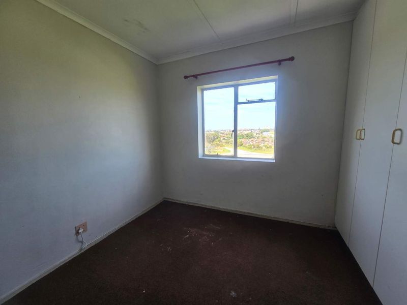 An empty bedroom featuring built-in cupboards, carpeted flooring, and a window with a view of the surrounding neighbourhood.