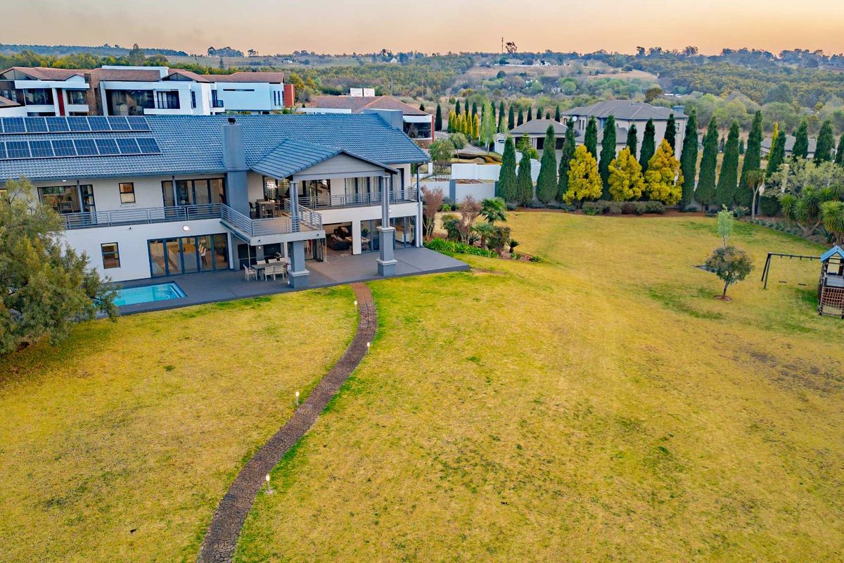 Aerial view of a large residential property featuring a spacious lawn, swimming pool, covered patio, balcony, and solar panel installation on the roof.