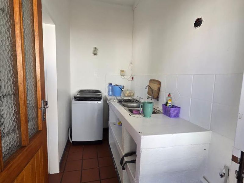 A functional laundry area featuring a built-in concrete counter, stainless steel sink, and durable terracotta floor tiles.