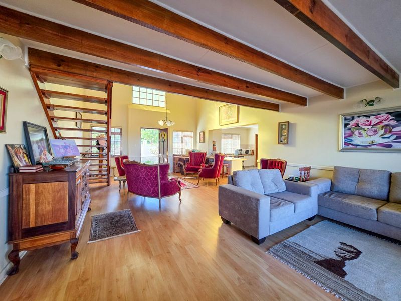Spacious open-plan living area featuring exposed timber ceiling beams, a feature timber staircase, and double-volume ceilings with abundant natural light.