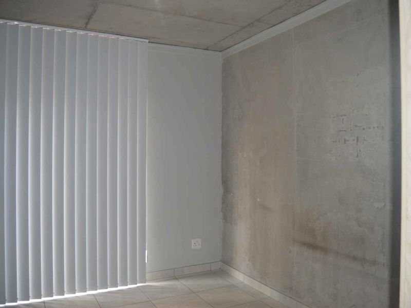 An empty bedroom featuring tiled flooring, vertical blinds, and an exposed concrete ceiling with an unfinished wall surface.