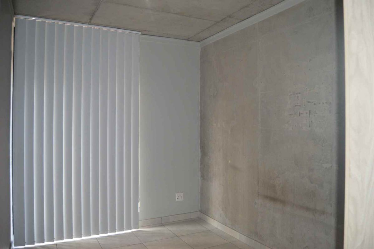 An empty bedroom featuring tiled flooring, vertical blinds, and an exposed concrete ceiling with an unfinished wall surface.