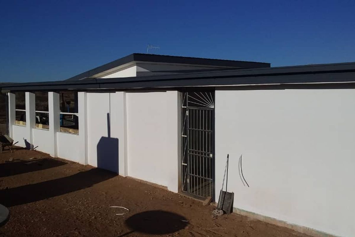 Rear exterior view of the farm property featuring a covered patio area, security gate, and freshly painted white walls under a modern roof structure.