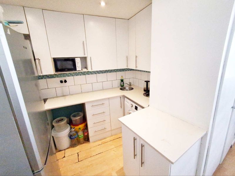 Compact kitchen featuring white cabinetry, tiled backsplash, built-in microwave, and laminate countertops, providing a functional workspace.