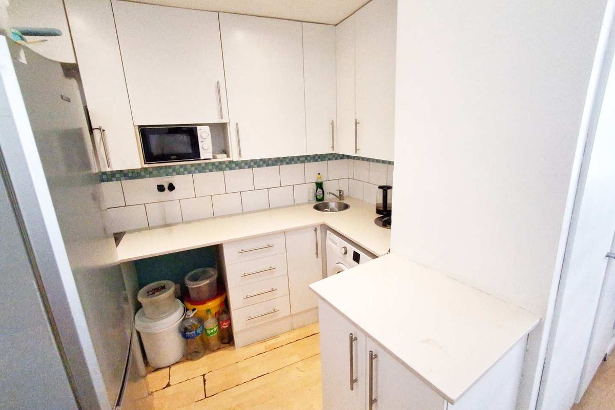 Compact kitchen featuring white cabinetry, tiled backsplash, built-in microwave, and laminate countertops, providing a functional workspace.
