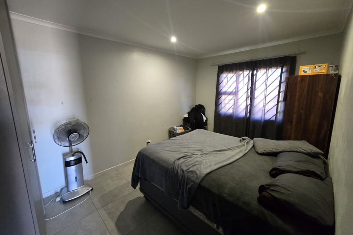 A functional bedroom featuring tiled flooring, recessed ceiling lighting, and security bars on the window.
