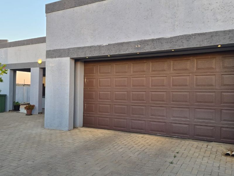 A modern residential garage featuring a brown sectional door, recessed exterior lighting, and a paved driveway area.