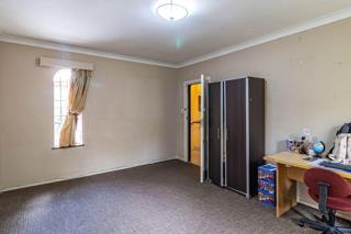 A bedroom featuring neutral wall tones, carpeted flooring, a window with security bars, and a built-in cupboard.