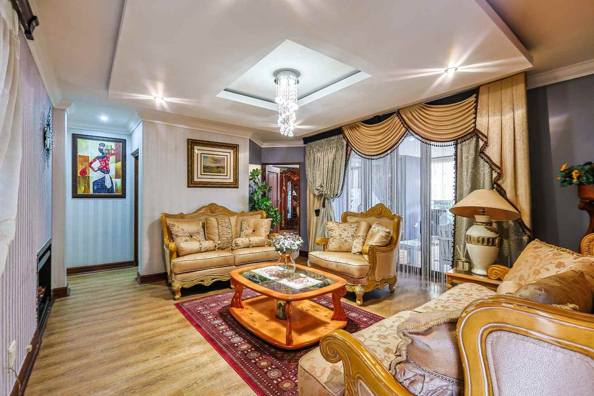 A formal living room featuring a recessed tray ceiling with integrated downlights, a central crystal chandelier, and wood-look flooring.