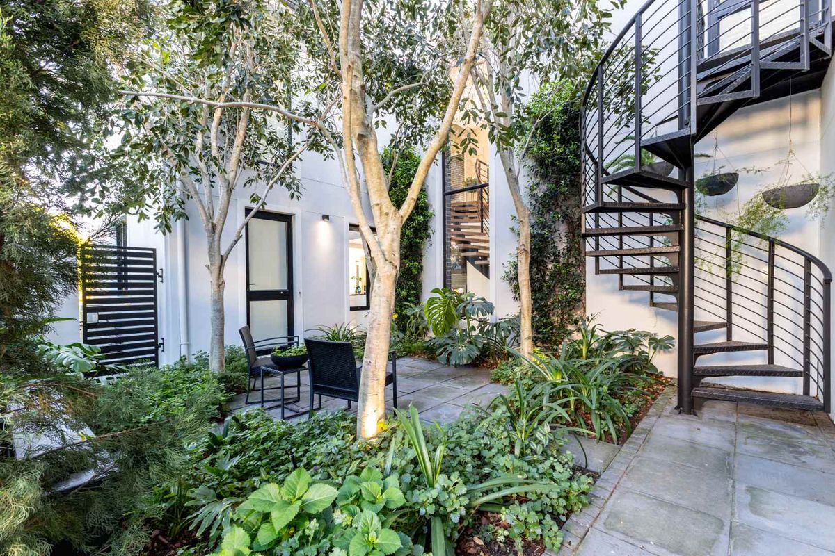 A beautifully landscaped rear courtyard featuring stone paving, lush greenery, and a striking black metal spiral staircase leading to an upper level.