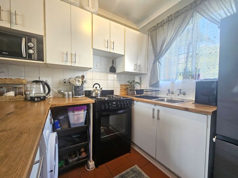 A functional kitchen featuring white cabinetry, wood-look countertops, a tiled backsplash, and a freestanding oven, offering a practical layout for daily meal preparation.