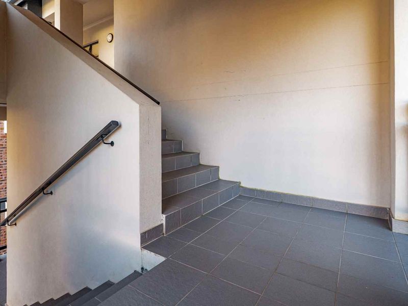 A functional apartment building hallway featuring a tiled staircase with a metal handrail and neutral wall finishes.