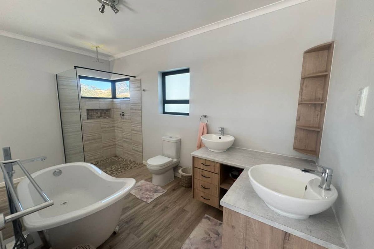 Modern bathroom featuring a freestanding bathtub, walk-in shower with tiled accents, and a dual vanity with vessel sinks and built-in shelving.