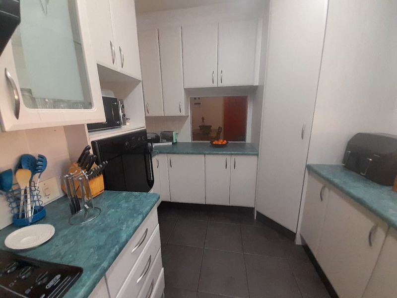A functional kitchen featuring white cabinetry, teal laminate countertops, built-in oven, and dark ceramic floor tiles with a convenient pass-through window.