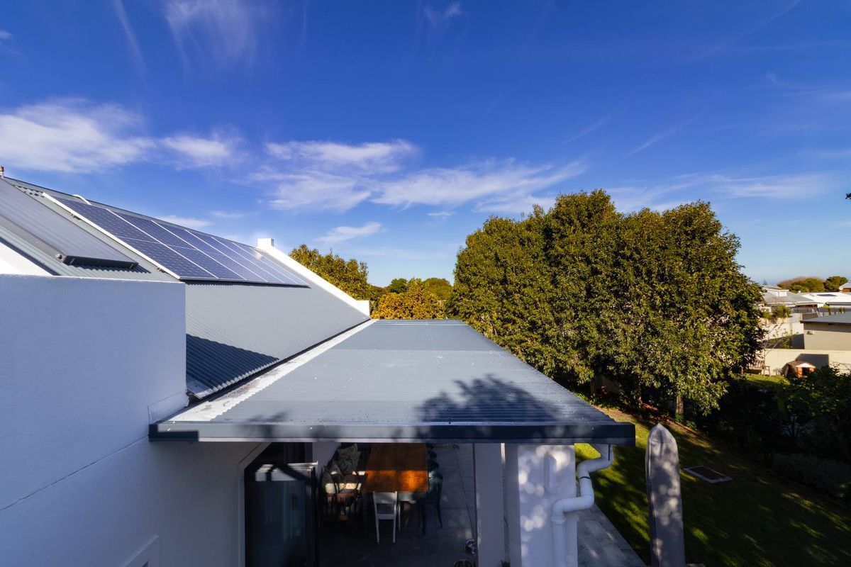 Elevated view of the rear property featuring a corrugated metal roof, integrated solar panels, and a covered patio area overlooking the garden.
