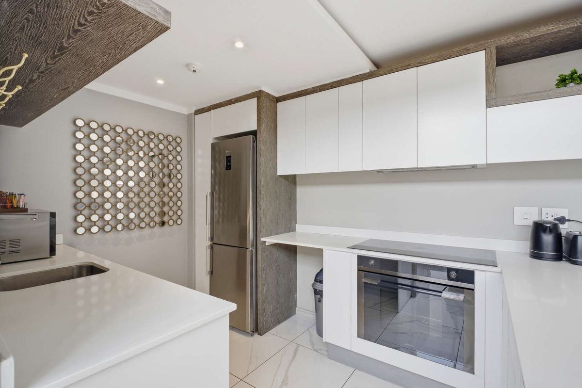 Modern kitchen featuring sleek white cabinetry, stone countertops, integrated oven, glass cooktop, and stainless steel refrigerator in a clean, contemporary penthouse setting.