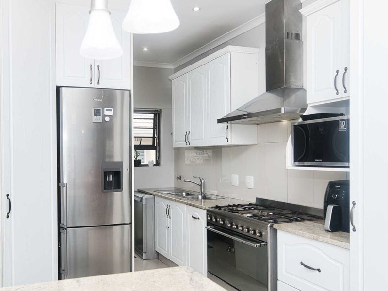 A well-maintained kitchen featuring white cabinetry, stone countertops, a stainless steel gas stove with extractor fan, and a double sink with tiled backsplash.