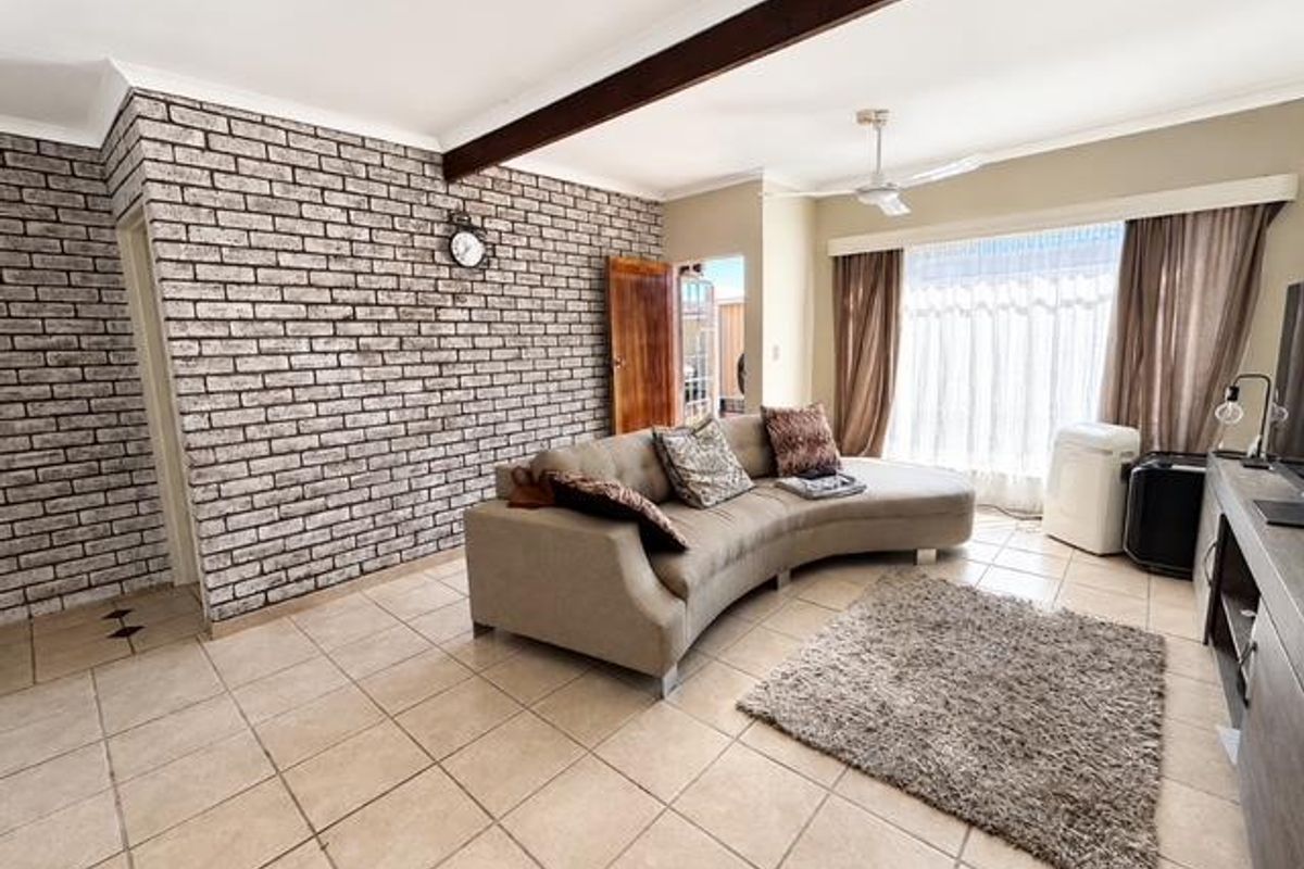 Spacious living room featuring an exposed brick accent wall, ceramic tile flooring, and a prominent timber ceiling beam, offering a comfortable and character-filled living space.