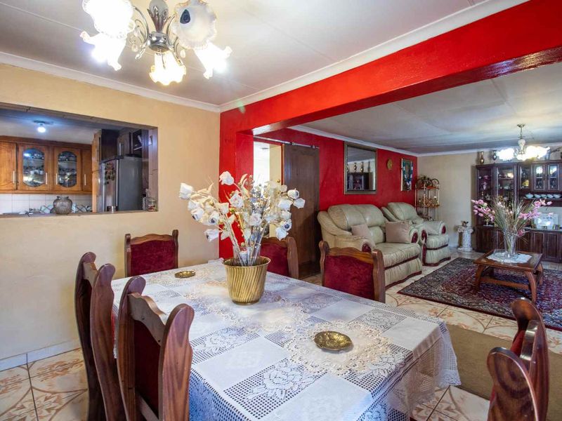 Open plan living and dining area featuring ceramic floor tiles, a pass-through window to the kitchen, and decorative ceiling coving.