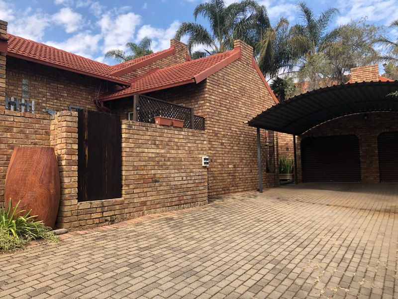 Front exterior view of a face brick house featuring a paved driveway, double garage, and a covered carport area.