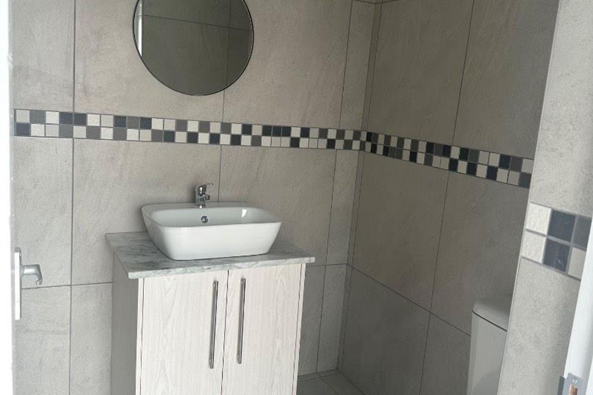 A modern guest bathroom featuring large format grey wall tiles, a vanity cabinet with a vessel sink, and a standard toilet.