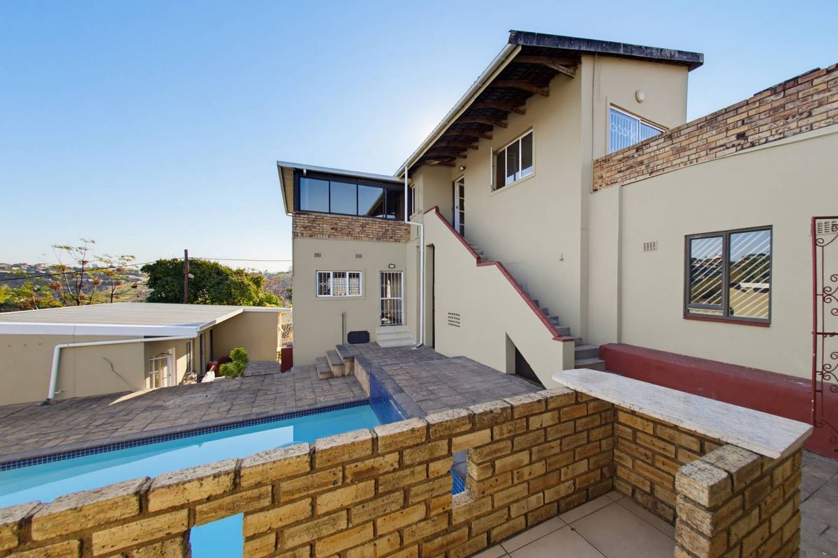 Rear exterior view featuring a swimming pool, paved patio area, external staircase, and brick boundary wall with a built-in stone counter.