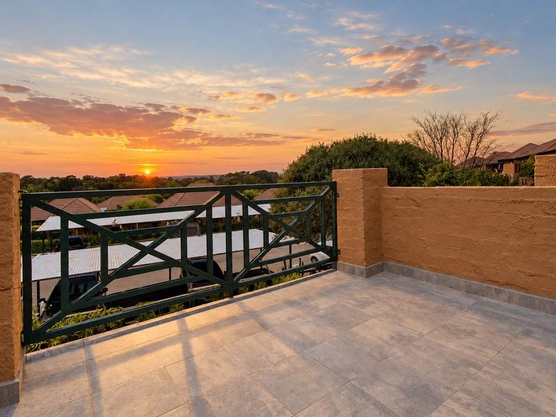 A spacious balcony featuring tiled flooring and a metal balustrade, offering scenic sunset views over the surrounding residential area.