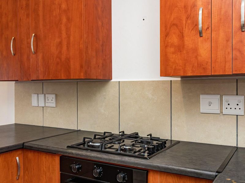 A functional kitchen area featuring wood-finish cabinetry, a built-in gas hob, an oven, and a neutral tiled splashback with ample countertop workspace.