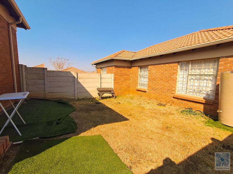A rear garden area featuring a brick exterior, tiled roof, and precast concrete boundary wall, with an external geyser unit installed.