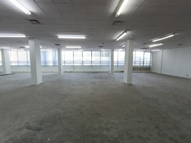 A large, open-plan office space featuring a suspended ceiling, structural columns, and expansive windows with vertical blinds, ready for custom fit-out.