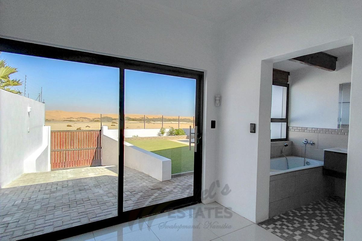A bright bedroom featuring large sliding glass doors opening to a private patio and garden, with an adjoining en-suite bathroom.