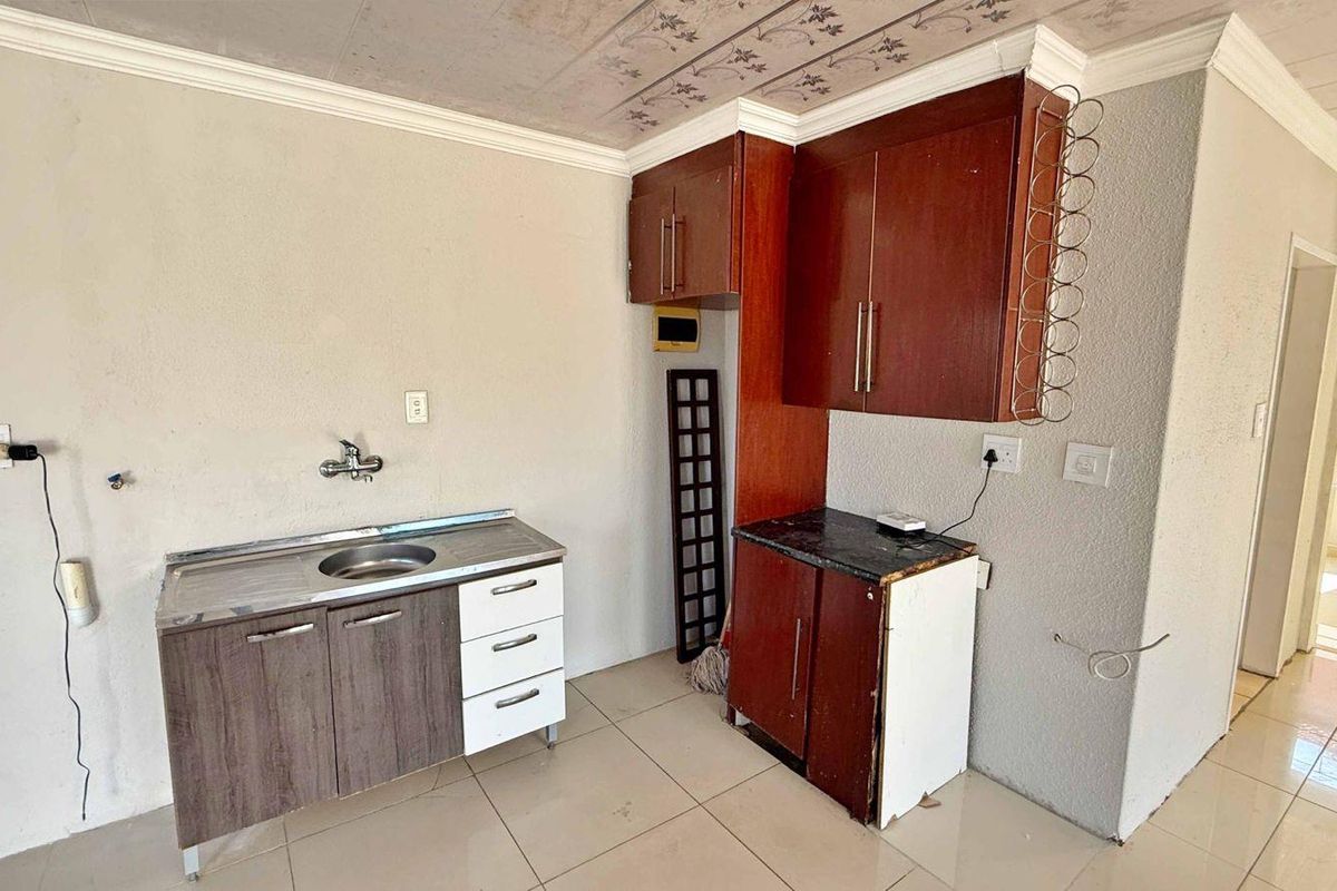 A compact kitchen area featuring basic cabinetry, a stainless steel sink, and tiled flooring, offering a functional space ready for modernization.