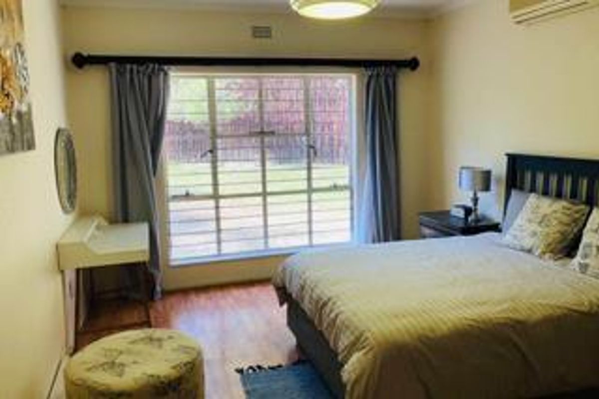 A bedroom featuring laminate flooring, a large window with security bars, and a wall-mounted air conditioning unit.