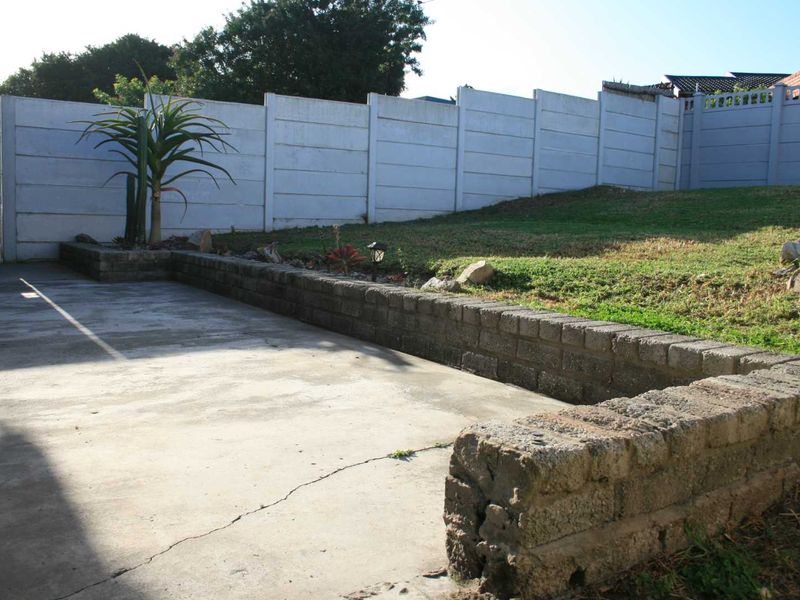 Rear garden area featuring a concrete patio, tiered retaining walls, and a secure precast boundary wall.