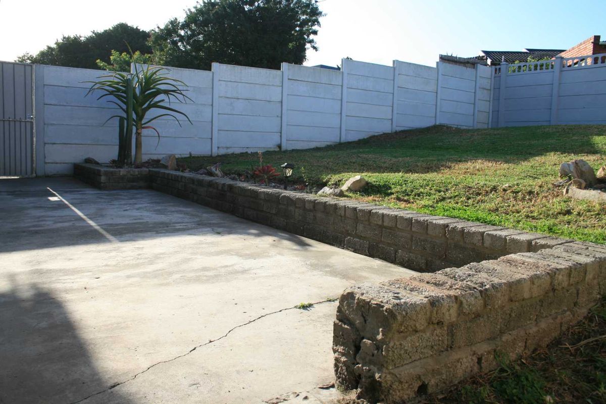 Rear garden area featuring a concrete patio, tiered retaining walls, and a secure precast boundary wall.