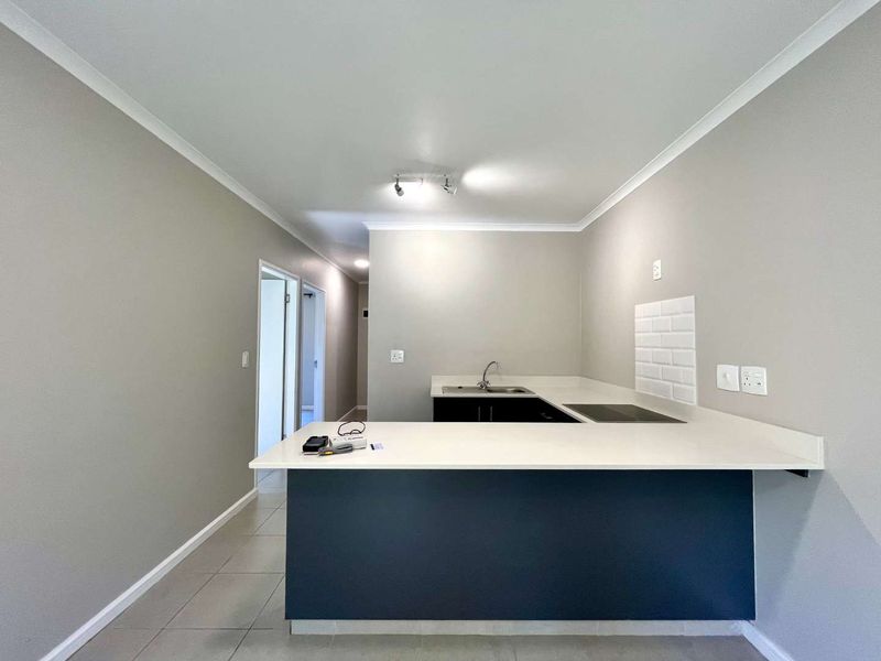 A clean, modern kitchen featuring a breakfast bar, built-in hob, sink, and subway tile backsplash with neutral wall finishes.